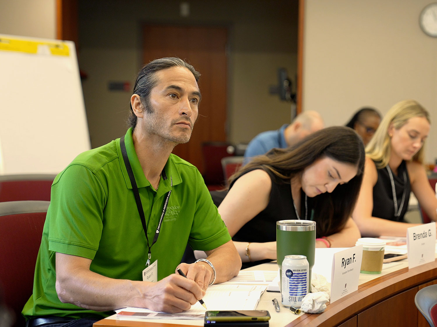 Program participants sit at a desk, listening to a speaker.