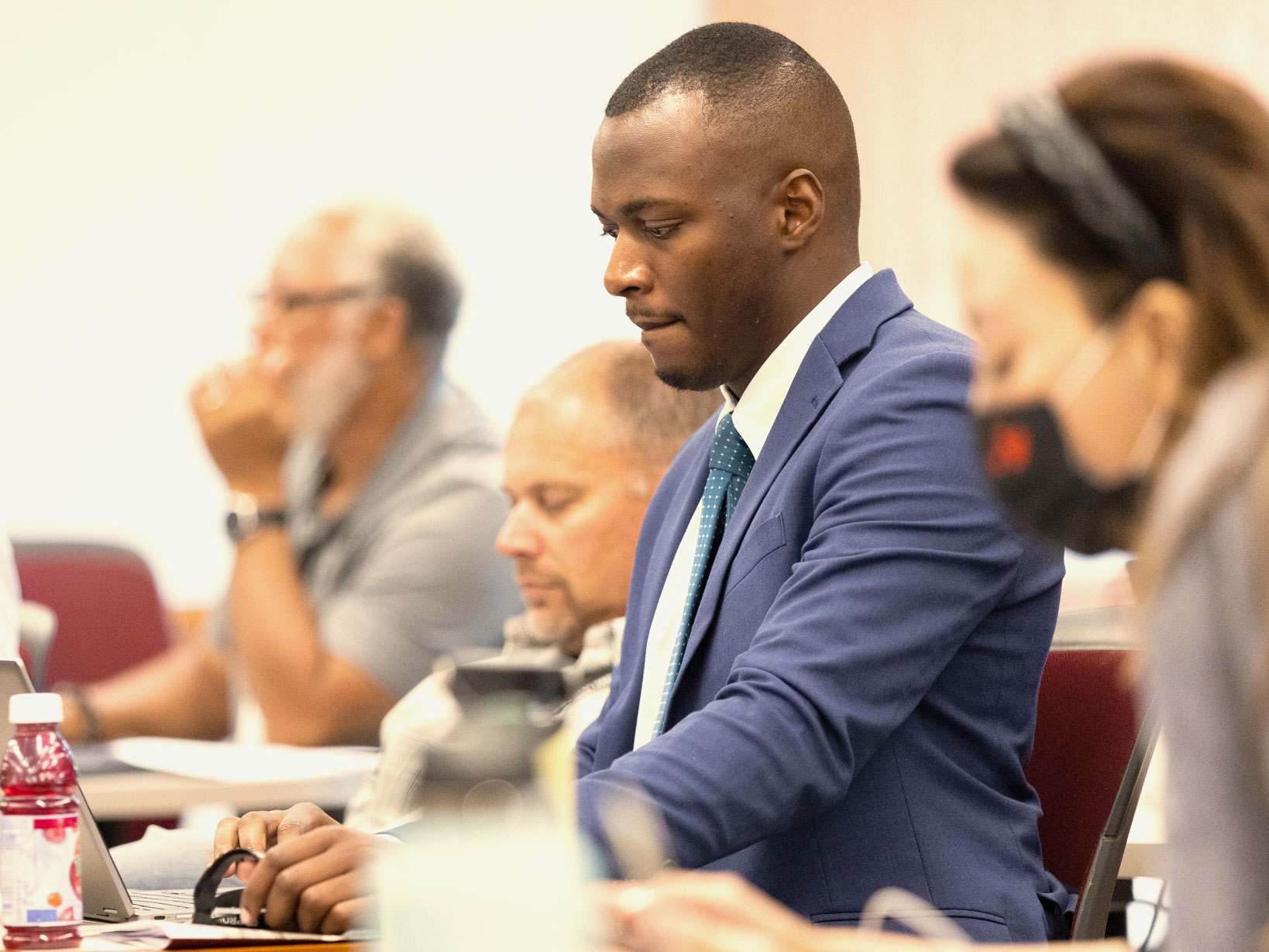 A man in a blue suit listens intently during a classroom session while typing on a computer.