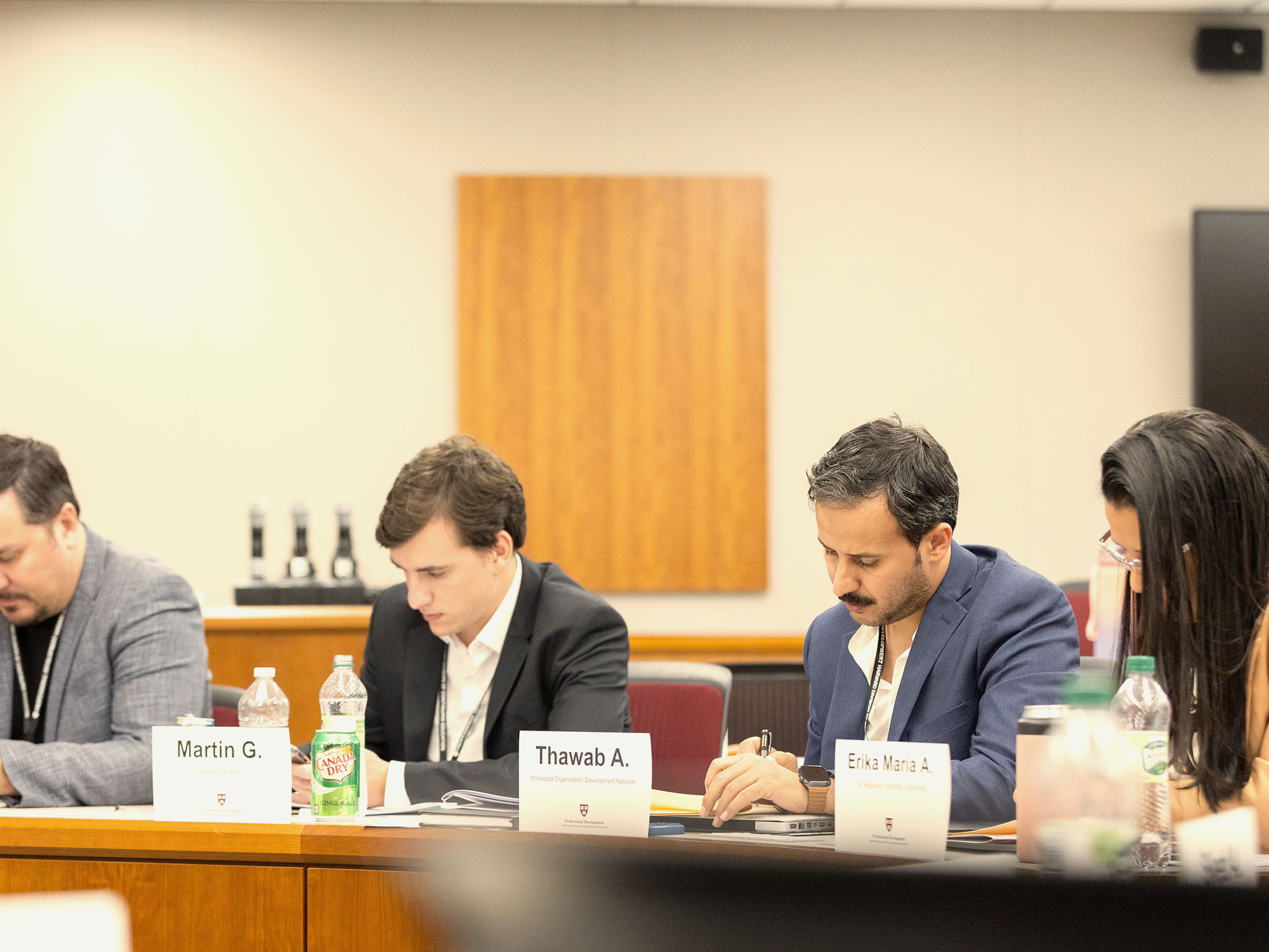 Four people sit at a table writing during a classroom session.