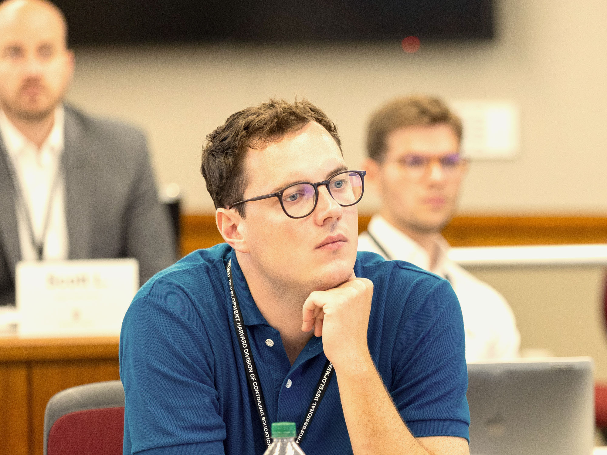A man in a classroom setting with glasses staring intently with his hand on his chin