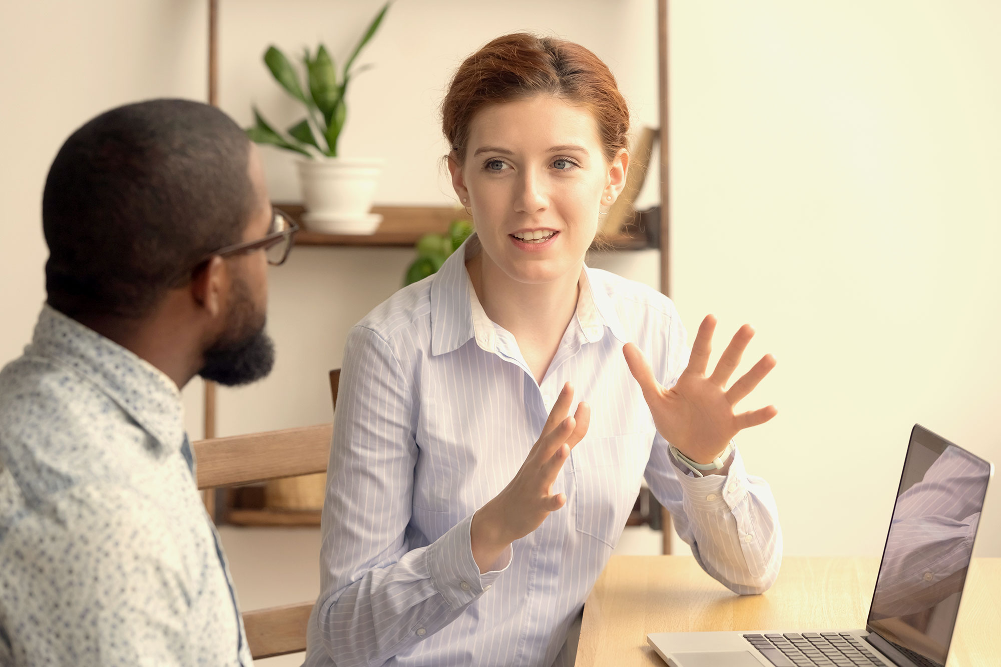 A woman gestures with her hands as she speaks to a man at a desk. Image for gender promotion gap.