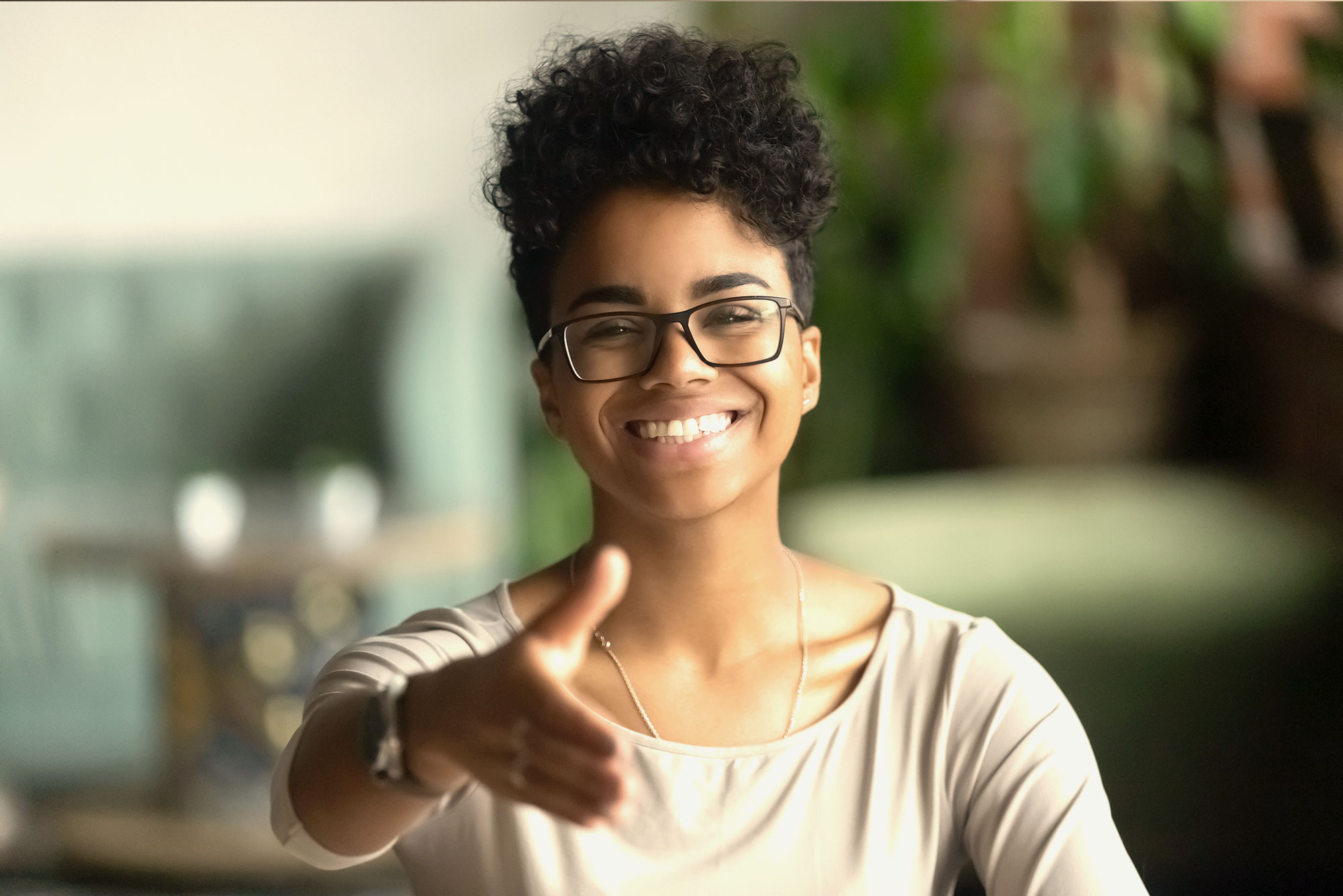 A young Black woman smiles confidently while extended her hand for a handshake. Women Negotiation Skills.